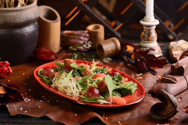 Salad with meat, grapes and orange. In a red plate. African decor