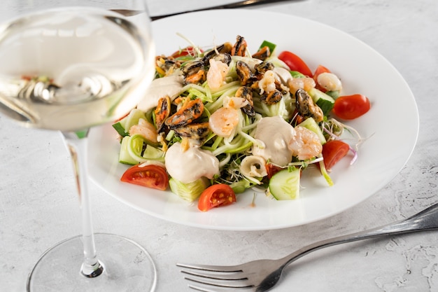 Salad with mussel, shrimp, tomato cherry, cucumber, zucchini pasta, microgreen, yogurt sauce on white plate on light table.