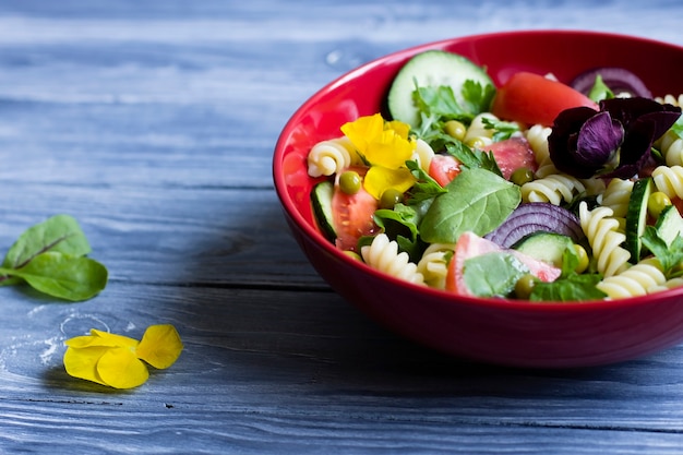 Salad with pasta and fresh vegetables. In a red plate.