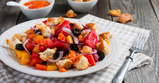 Salad with peppers, tomatoes, onions, olives and croutons with sousomna old wooden background. Selective focus.