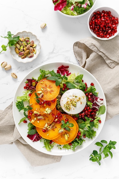 Salad with persimmon burrata pomergranat and pistachio healthy food top view