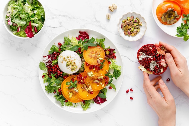 Salad with persimmon burrata pomergranat and pistachio healthy food top view