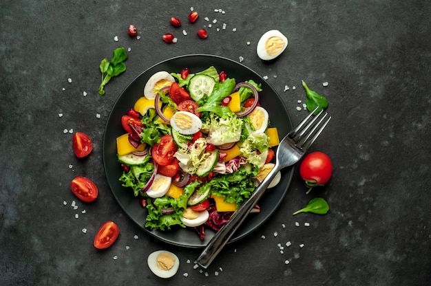 Salad with pomegranate, tomatoes, fresh cucumbers, onions, sesame seeds and cashew nuts, spices on a stone background. Healthy vegetarian food.