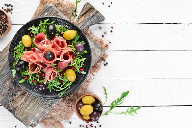 Salad with Prosciutto, olives and arugula. Cold snacks. Top view. Free space for your text.