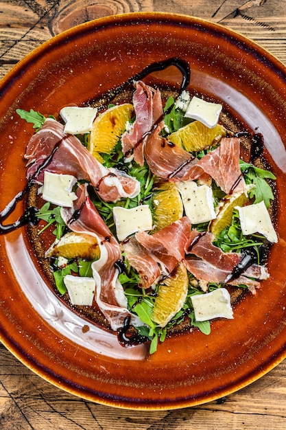 Salad with prosciutto parma ham, parmesan cheese, arugula and tangerine on a plate. wooden table. Top view.
