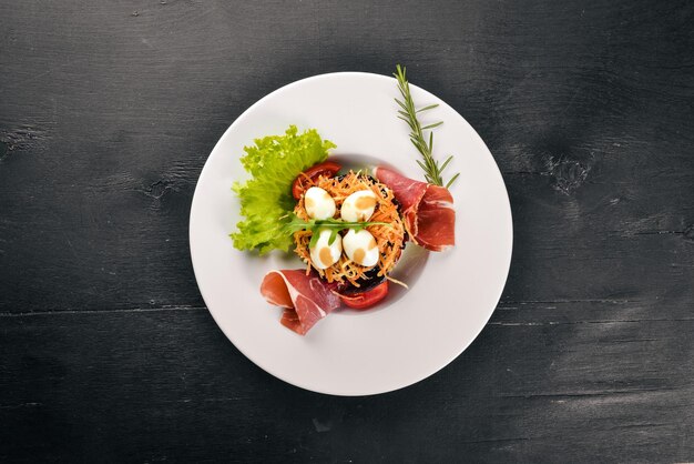 Salad with prosciutto quail eggs prunes and fresh vegetables on the plate On a wooden background Top view Free space for text