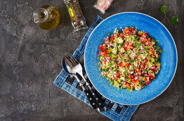 Salad with quinoa, arugula, sweet peppers, tomatoes and cucumber in bowl on a dark table. healthy food, diet, detox and vegetarian concept. tabbouleh salad. top view. flat lay