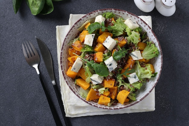 Salad with quinoa, pumpkin and dor blue cheese in a plate on a dark surface. view from above