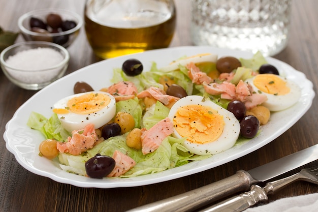 Salad with salmon, eggs and olives on white dish