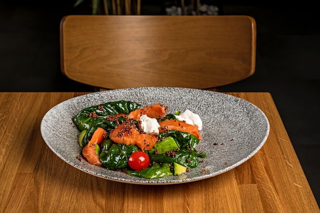 Salad with salmon kale avocado cherry tomatos and quinoa served on a grey plate on a wooden table in a restaurant