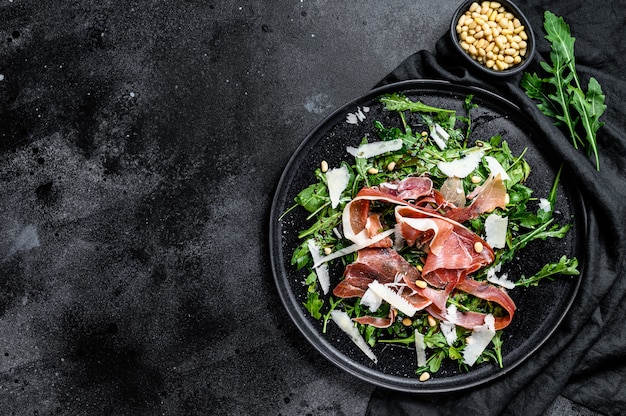 Salad with Serrano jamon, ham, rucola and Parmesan cheese. Black background, top view, space for text