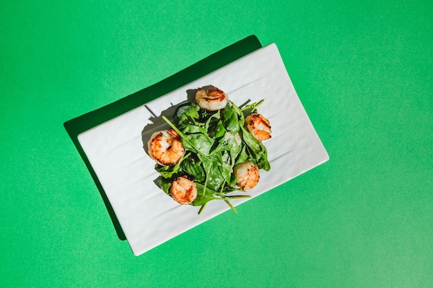 Salad with shrimps and arugula on white dish on colored background