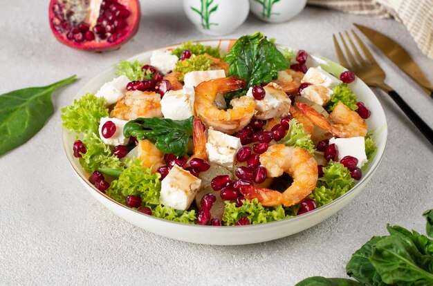 Salad with shrimps pineapple feta and pomegranate seeds in a plate on green lettuce leaves on a gray background