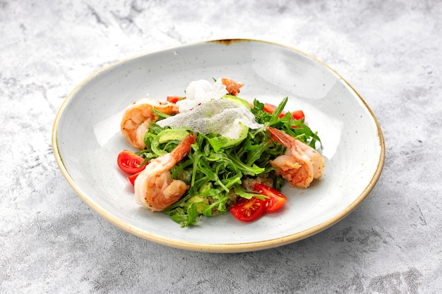 Салат с креветками, помидорами и рукколой, на белой тарелке, на светлом фоне