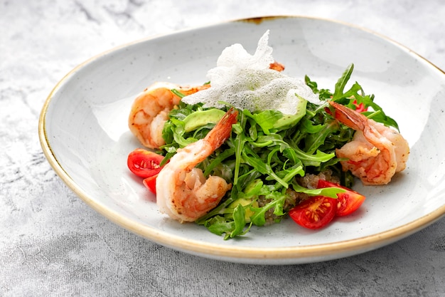 Salad with shrimps, tomatoes and arugula, on a white plate, on a light background