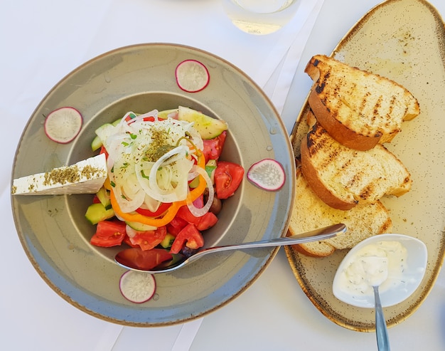 Salad with tomato, cucumbers, white onions, radishes, olives and feta on a gray plate. 