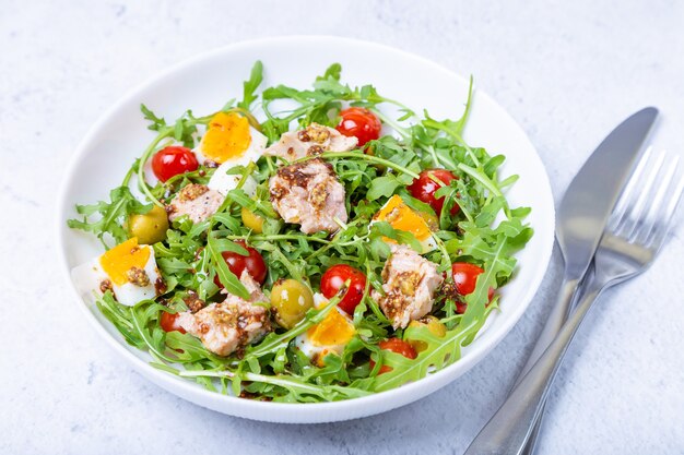 Salad with tuna, arugula, tomatoes, olives and eggs in a white plate. A traditional dish. Close-up.