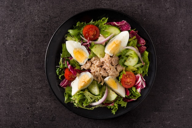 Salad with tuna, egg and vegetables on black background top view