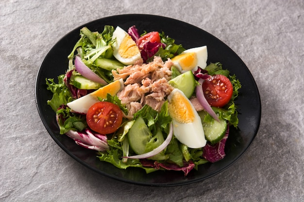 Salad with tuna, egg and vegetables on black plate and gray surface