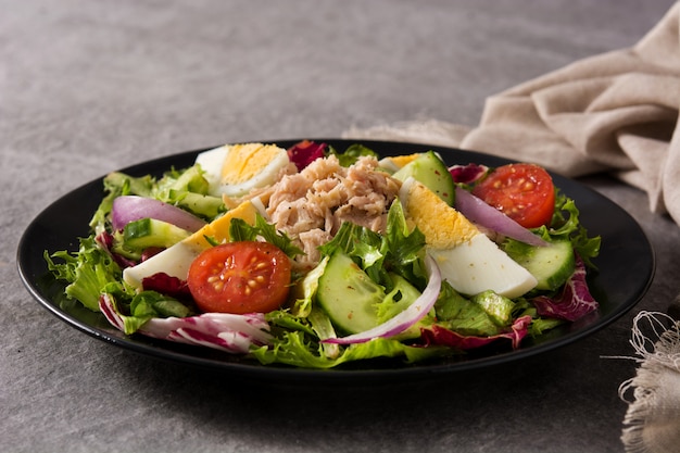 Salad with tuna, egg and vegetables on black plate and gray