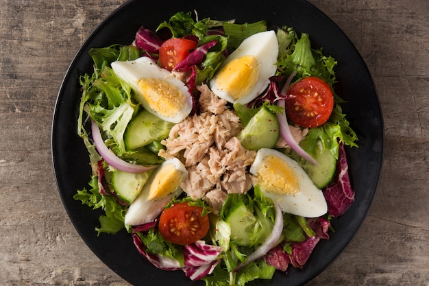 Salad with tuna, egg and vegetables on black plate and wooden table