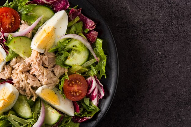 Salad with tuna, egg and vegetables on black