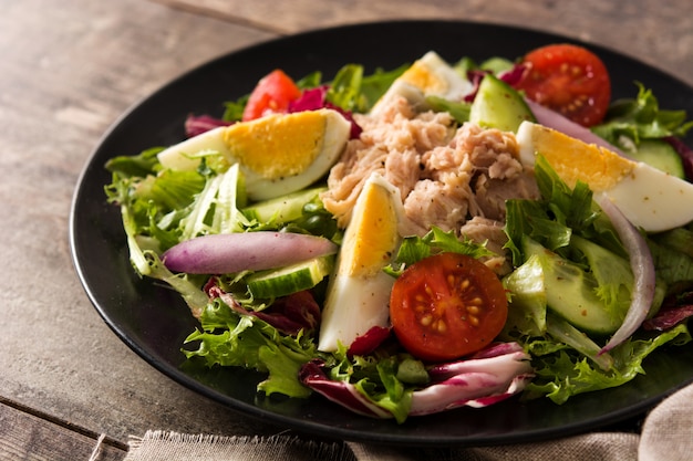Salad with tuna, egg and vegetables on wooden table