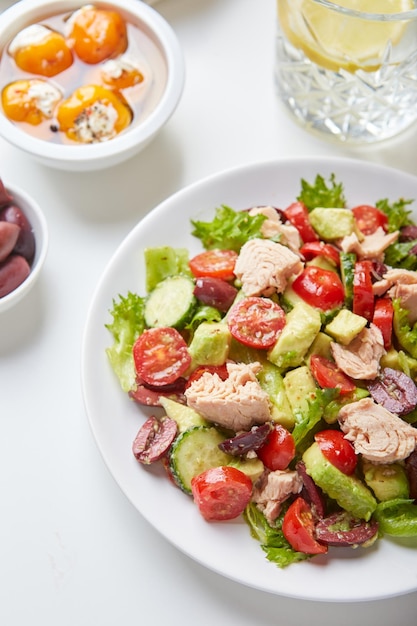 Salad with tuna lettuce cucumbers tomatoes olives and avocados in white plate on the table