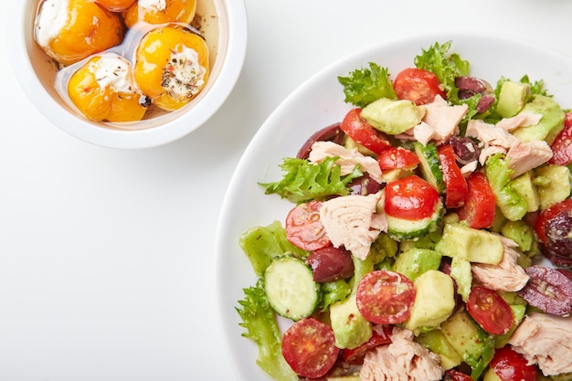 Salad with tuna lettuce cucumbers tomatoes olives and avocados in white plate on the table