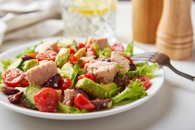 Foto insalata con tonno lattuga cetrioli pomodori olive e avocado in piatto bianco sul tavolo