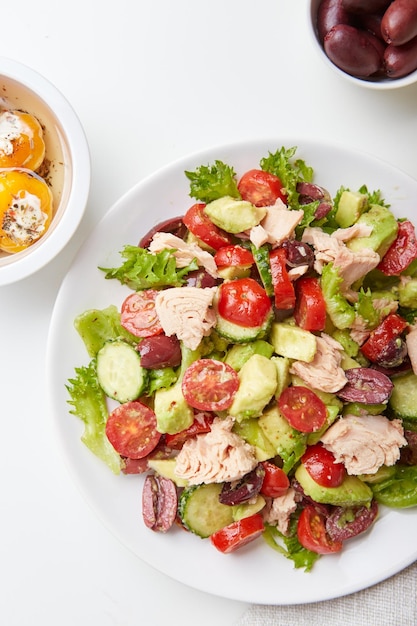 Salad with tuna lettuce cucumbers tomatoes olives and avocados in white plate on the table