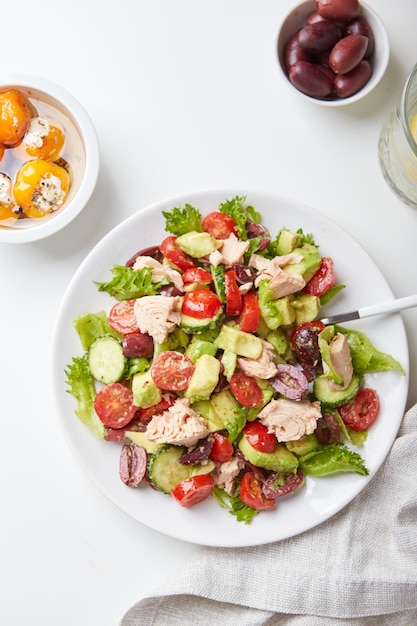 Insalata con tonno lattuga cetrioli pomodori olive e avocado in piatto bianco sul tavolo