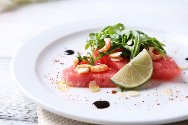 Salad with watermelon feta arugula shrimps balsamic sauce on plate on wooden background