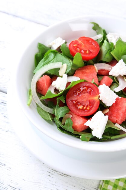 Salad with watermelon onion arugula and spinach leaves on plate on wooden background