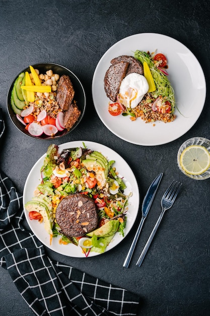 Salade en kom met sappig plantaardig vlees avocado ei tomaat amandel greens quinoa radijs baby maïs quinoa gepocheerd ei komkommer en wortel donkere betonnen achtergrond bovenaanzicht