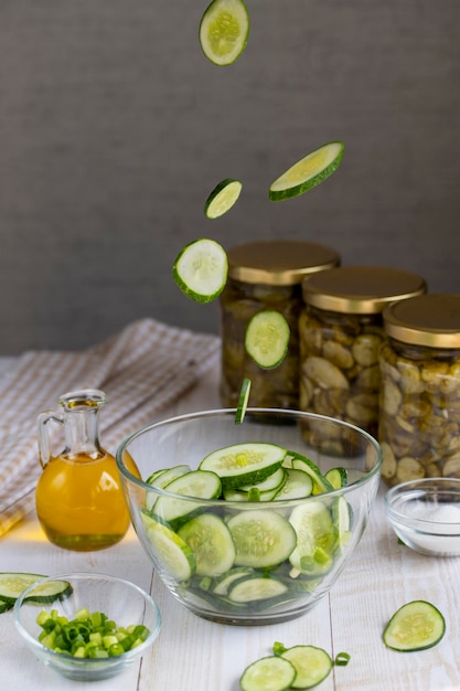 Salade koken met verse komkommers Vliegende plakjes komkommer in een glasplaat voor salade op de achtergrond van ingeblikte komkommersalade in glazen potten