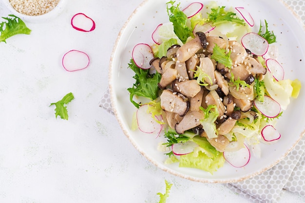 Salade koning oesterzwammen met sesamzaadjes, radijs en sla op een bord. Pleurotus eryngii. Bovenaanzicht