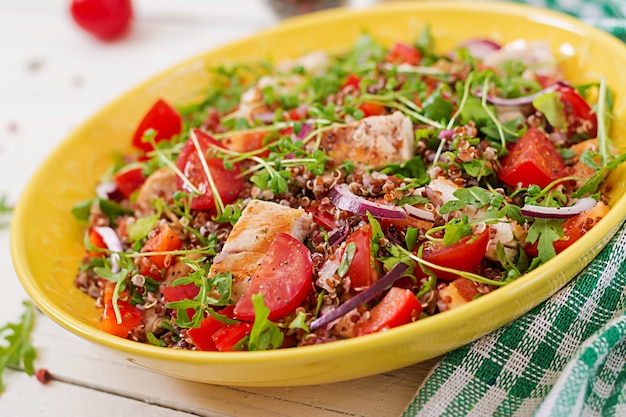 Salade lunch met gegrilde kip en quinoa, tomaat, paprika, rode uien en rucola op wit.