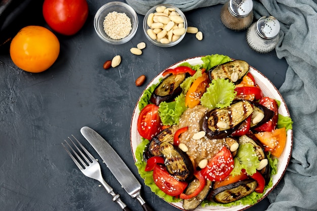 Salade met aubergine, tomaat, paprika, sla, sesam en pinda's, bovenaanzicht op donker,