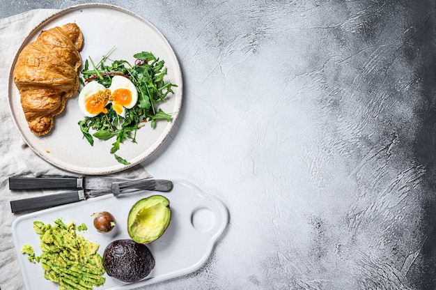 Salade met avacado, rucola, croissant en ei. Grijze achtergrond. Bovenaanzicht. Ruimte voor tekst