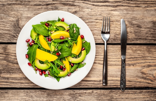 salade met avocado, rucola, spinazie, granaatappel, zaden op houten achtergrond