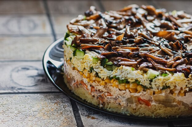 Salade met champignons, eieren, likdoorns en wortelen op de plaat op rustieke betegelde tafel.