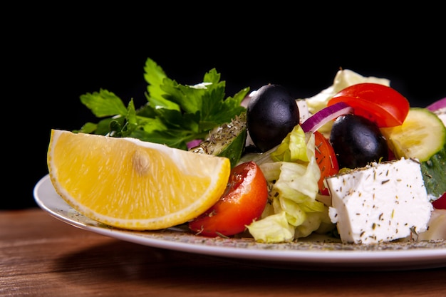 Salade met feta-kaas, olijven, sla, tomaten, komkommer, citroen op zwarte achtergrond.