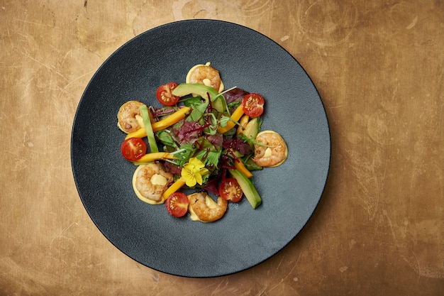 Foto salade met gebakken garnalen, rucola, cherrytomaatjes, avocado en mango in een zwarte keramische plaat