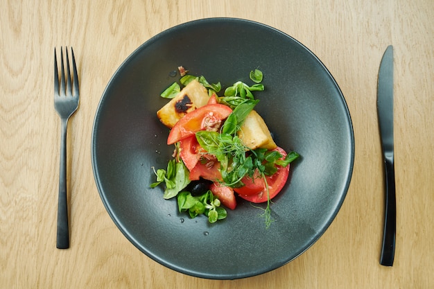 Salade met gebakken halumi kaas cherry tomaten en microgreen in zwarte kom op houten tafel. Restaurant eten