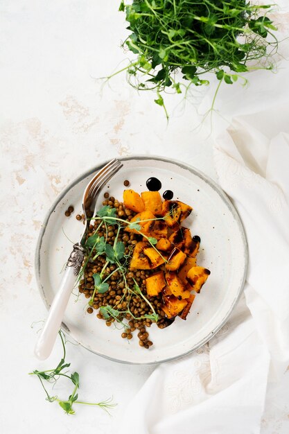 Salade met gebakken pompoen, linzen en balsamico dressing gegarneerd met erwten microgreens op een lichtje