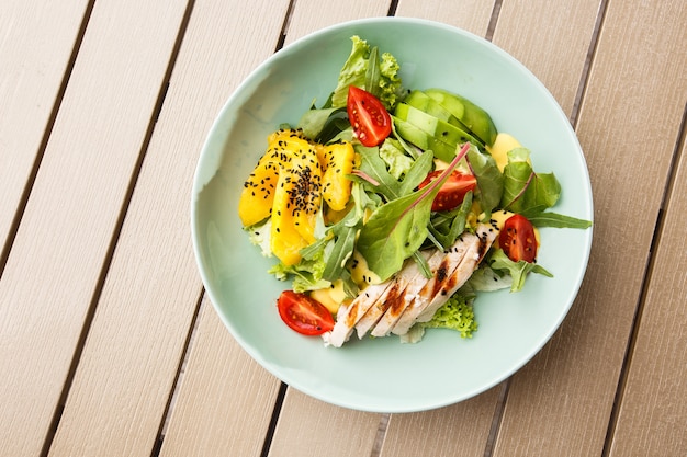 Salade met gegrilde kip, mango, sla, avocado, tomaten, rucola, kaas saus op een witte plaat