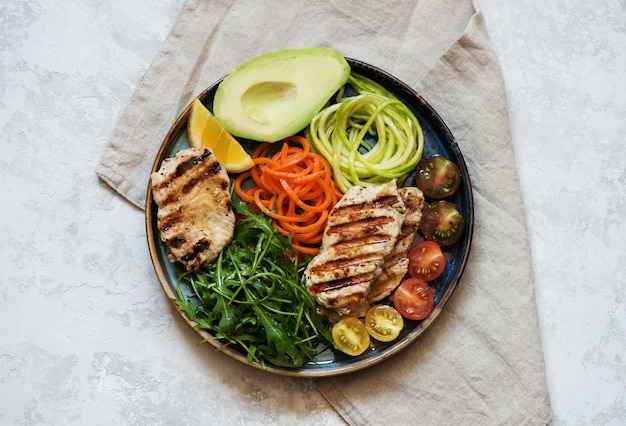 Salade met gegrilde kipfilet, rucola, avocado, wortelen en courgette, uitgebalanceerd schoon eten, bovenaanzicht. Gezonde lunchkom.