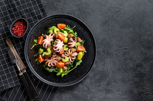 Salade met gegrilde octopus, aardappelen, rucola, tomaten en olijven. Zwarte achtergrond. Bovenaanzicht. Ruimte voor tekst
