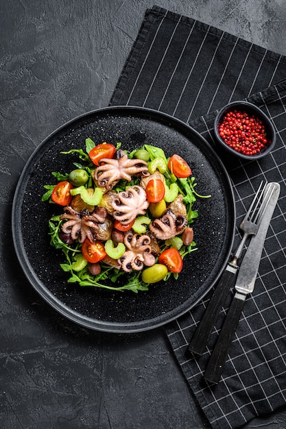 Salade met gegrilde octopus, aardappelen, rucola, tomaten en olijven. Zwarte achtergrond. Bovenaanzicht